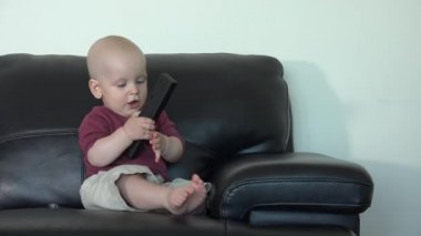 Caucasian boy sit on sofa with remote control. Cheerful child have fun at home