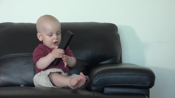 Caucasian boy sit on sofa with remote control. Cheerful child have fun at home — Stok video