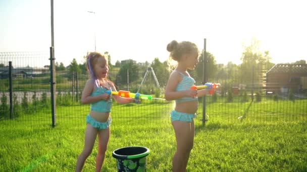 Chica pelirroja en traje de baño salpicando pistola de agua en amigos espalda. Hermanas refrescantes — Vídeo de stock