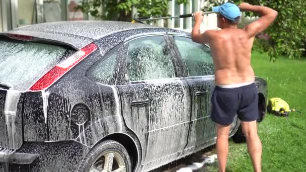 Tipo con escoba limpiando el techo de su automóvil en el patio de la casa — Vídeo de stock