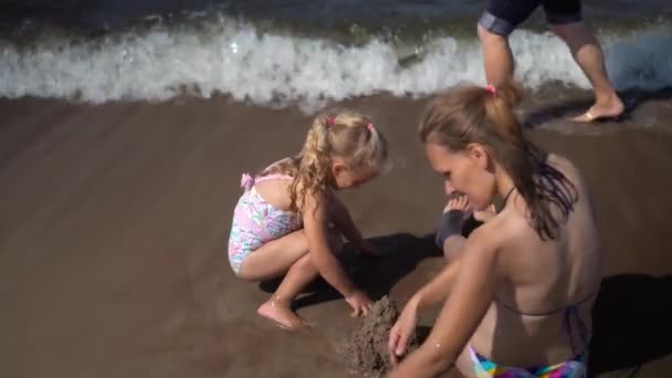 Мать и дочь строят и разрушают песчаный замок на пляже — стоковое видео