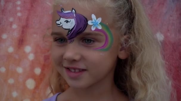 Chica emocionada disfrutar de la pintura en la cara. Pony arco iris pintado en la frente del niño — Vídeo de stock