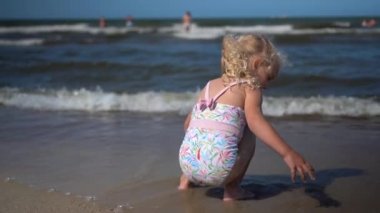 Güzel kız deniz dalgalarının yanında kumla oynuyor. Mayolu kadın çocuk iyi eğlenceler.