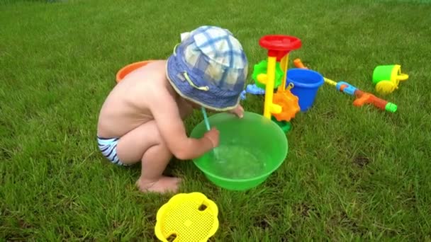 2 yaşında küçük bir çocuk sopayla hava üflüyor. Kabın içine su sıçrıyor. — Stok video