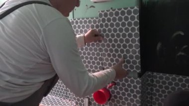 İşçi WC dolap çerçevesine fayanslar yerleştirir. Dolap bağlantısı için renkli borular