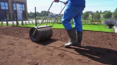 Adam çimlere tohum ekmeden önce toprağı hazırlamak için bir silindir kullanıyor. el bilgisayarı