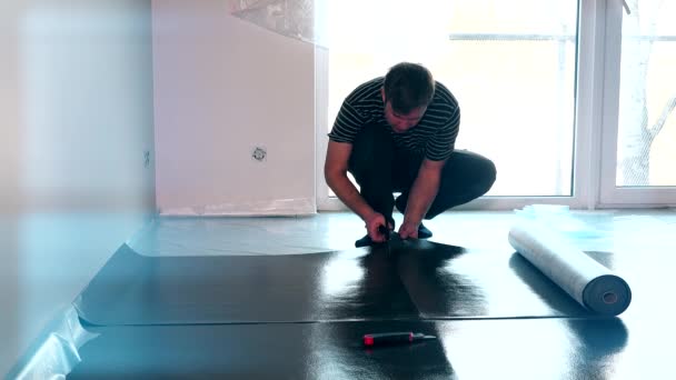 Muž s nůžkami stříhá podklad pro montáž laminátové podlahy — Stock video