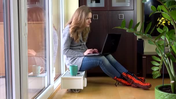 Nervös kvinna arbetar med datorn sitter på kylaren i rummet. 4K — Stockvideo