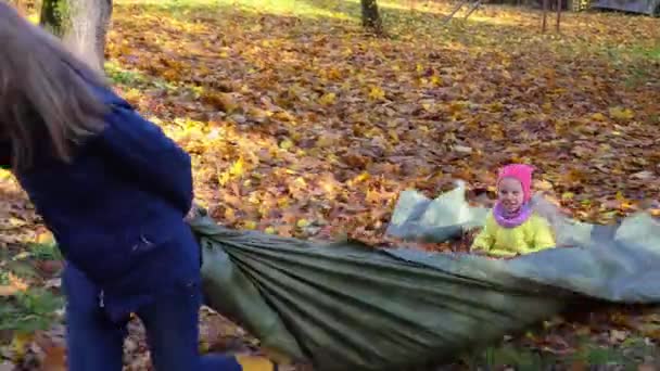 Lekfull mamma drar liten dotter med staplade löv på toppen av tältet — Stockvideo