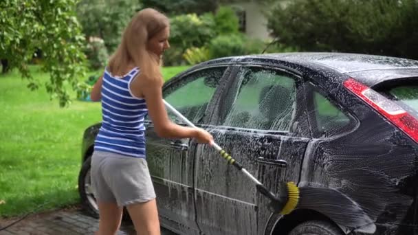Αυτόματη πλύση. Νεαρή ελκυστική ξανθιά γυναίκα σε σορτς πλύσιμο βρώμικο αυτοκίνητο στην ύπαιθρο — Αρχείο Βίντεο