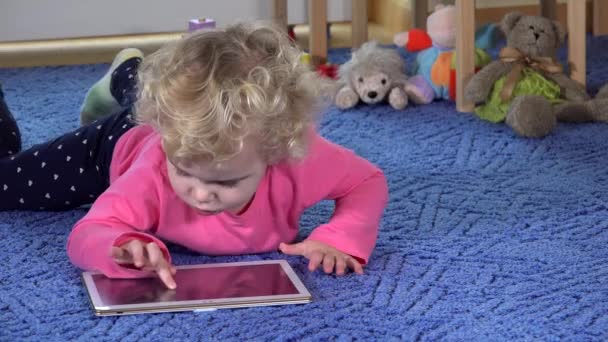 女の子は青いカーペットの上に横たわるタブレットを再生します。現代のメディア技術です。4K — ストック動画
