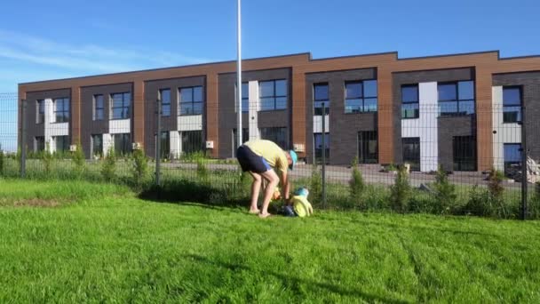 Καυκάσιος άντρας διδάσκει τον μικρό γιο να κόβει γρασίδι στον κήπο με μηχανή κουρέματος παιχνιδιών. Λαμπερή κίνηση — Αρχείο Βίντεο