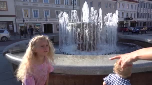 Hermana y hermano emocionados mirando el agua de la fuente que fluye hacia arriba. Disparo de mano — Vídeos de Stock