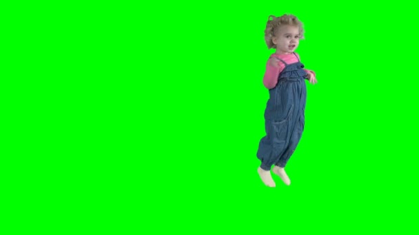 Krullend meisje springen in denim jumpsuit. Kind op groen scherm chroma key achtergrond. 4K — Stockvideo