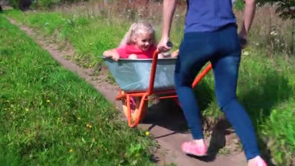 Feliz madre adulta joven e hija pequeña paseo rápido en carretilla de jardín — Vídeo de stock