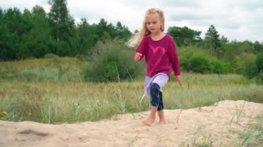 Mutlu güzel küçük kız, tapılası kıvırcık sarışın çocuk, kum tepelerinde yürüyor.