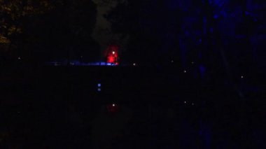 İnsanlar lazerle aydınlatılmış uzak şehir parkında yürüyor. 4K