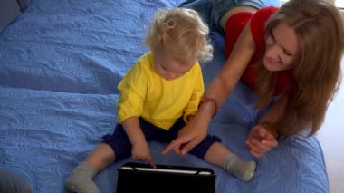 Anne ve bebek kanepede tablet kullanıyor. Eğitim, akıllı medya. 4K