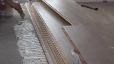 İşçi döşeme tahtası döşemesi için yerde spatula ile yapıştırıcı uygular