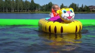 Kız çocuğu eğlence parkında havuzda şişme kaplan motorlu teknesine biniyor.