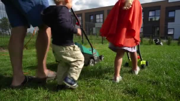 Father and Children mow lawn. daddy has real lawnmower, daughter a toy version — Stock Video