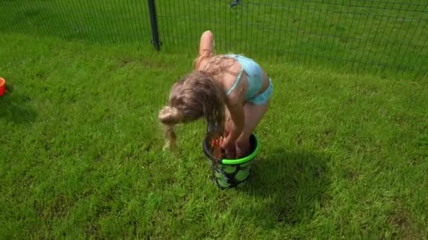 Blond girl with water gun standing in bucket chasing her dad in yard — Stock Video