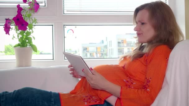 Gravid kvinna med surfplatta letar efter varor och betalar med bankkort — Stockvideo