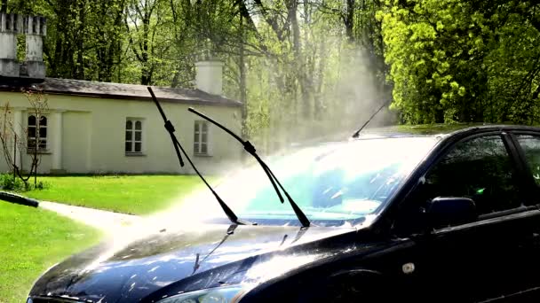 Mano masculina pulverizar alta presión de agua en el vidrio frontal del coche negro. 4K — Vídeo de stock