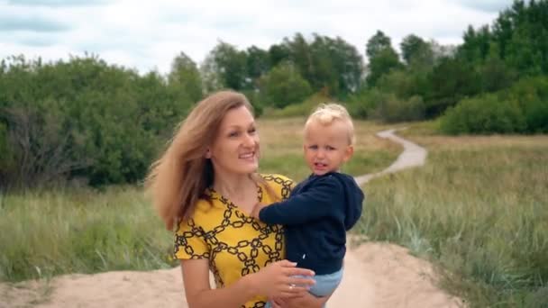 Ładna kobieta niesie dwa lata blondynka chłopiec w kierunku oceanu plaży — Wideo stockowe