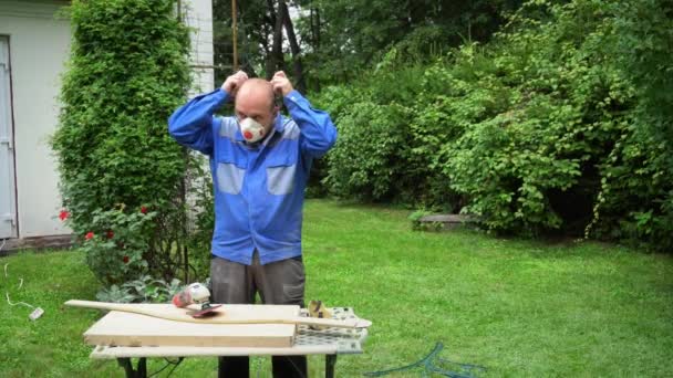 Timmerman zet beschermbril en masker op en start met het polijsten van hout boord — Stockvideo