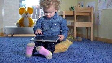 Kıvırcık kız tablet oynar mavi halıya oturur. Modern medya teknolojisi. 4K