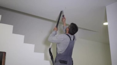 Man with handsaw sawing hole in gypsum ceiling for led light panel installation