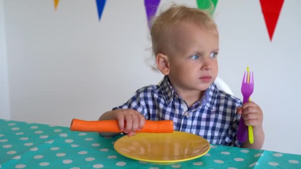 Ευτυχισμένο παιδί που κάθεται στο τραπέζι τρώγοντας φρέσκα λαχανικά καρότου. Λαμπερή κίνηση — Αρχείο Βίντεο