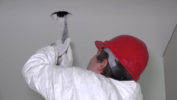 Hombre con casco rojo ampliar un agujero para una lámpara de iluminación led en el techo. 4K — Vídeos de Stock