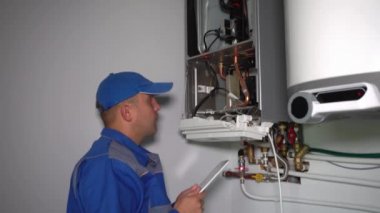 Bilgisayar sistemli teknisyen gaz kazanını ayarladı ve gülümsüyor.