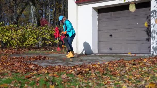 Pemilik rumah wanita membersihkan pintu masuk ke garasi mobilnya di musim gugur — Stok Video