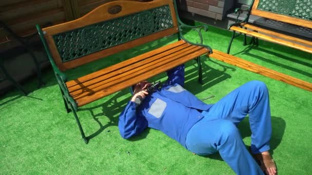 Handyman with electric screwdriver assemble bench furniture in house yard. — Stock Video