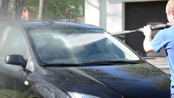 Рабочий человек моет лобовое стекло автомобиля с сильным давлением струи воды — стоковое видео