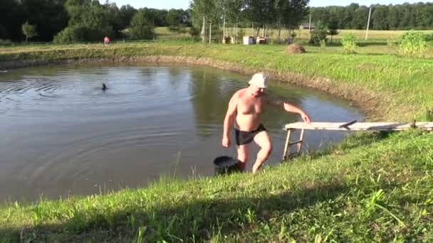 Gardener man draw water from pond with bucket and pour in tank — Stock Video