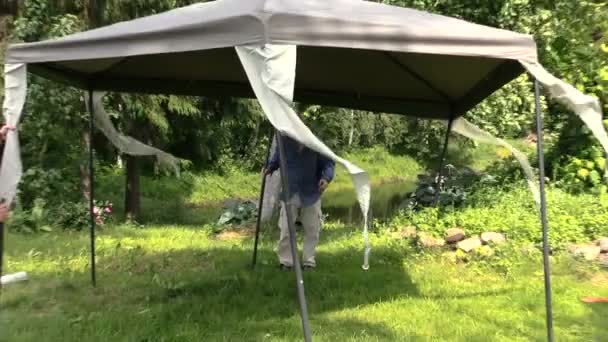Άνδρες σταθεροποίηση μεταλλικούς σωλήνες πλαίσιο πέργκολα με καμβά από βροχή — Αρχείο Βίντεο