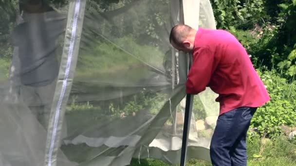 Man bind to arbor bar mosquito screen on windy day, tilt down. — Stock Video