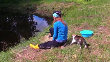 Hamile kız göl kıyısında oturmak ve şirin kedi ile balık yakalamak