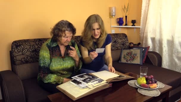 Бабушка показывает внучке фотографии из альбома молодого времени — стоковое видео