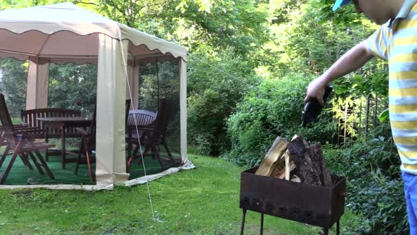 Man häller bränsleblandningen på ved och ljus eld med brännare — Stockvideo