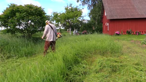 Bărbat cu tuns tăiat iarbă înaltă în curtea casei de origine rurală — Videoclip de stoc