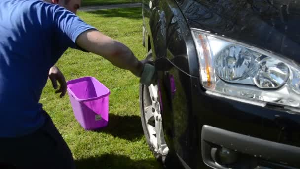 Man wassen zijn favoriete auto wielen met spons water en zeep op gazon. — Stockvideo