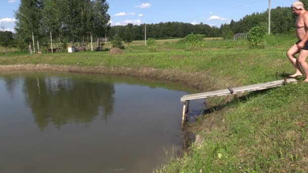 Men and girl jump in turn in pond from footbridge on countryside — Stock Video