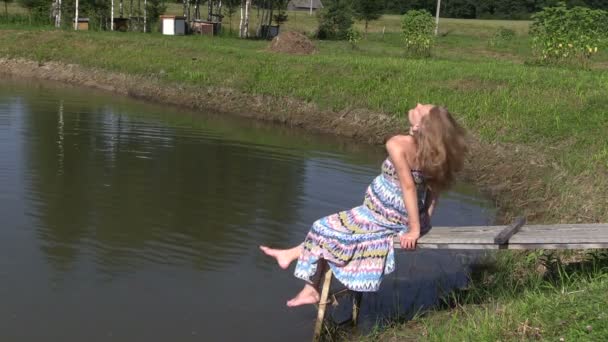 Mulher grávida em vestido longo sentar na ponte de madeira perto da lagoa — Vídeo de Stock