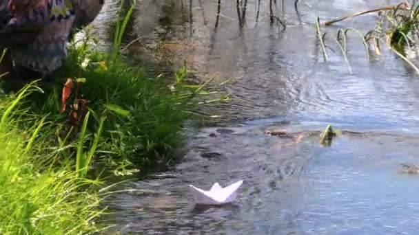 Fille tourner bateau en papier blanc près de la rive du ruisseau dans le parc vert 