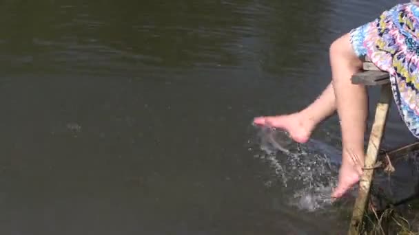 Беременная женщина сидит на мосту и брызгает водой пруд с ногами — стоковое видео